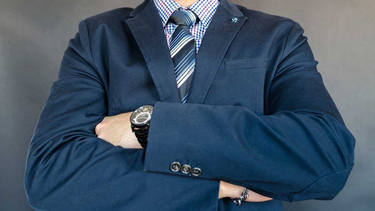 closeup of main in blue business suit with arms crossed, looking strong.