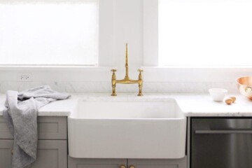 White and grey kitchen cupboards, marble kitchen countertop and white farm sink with two big kitchen windows behind the sink