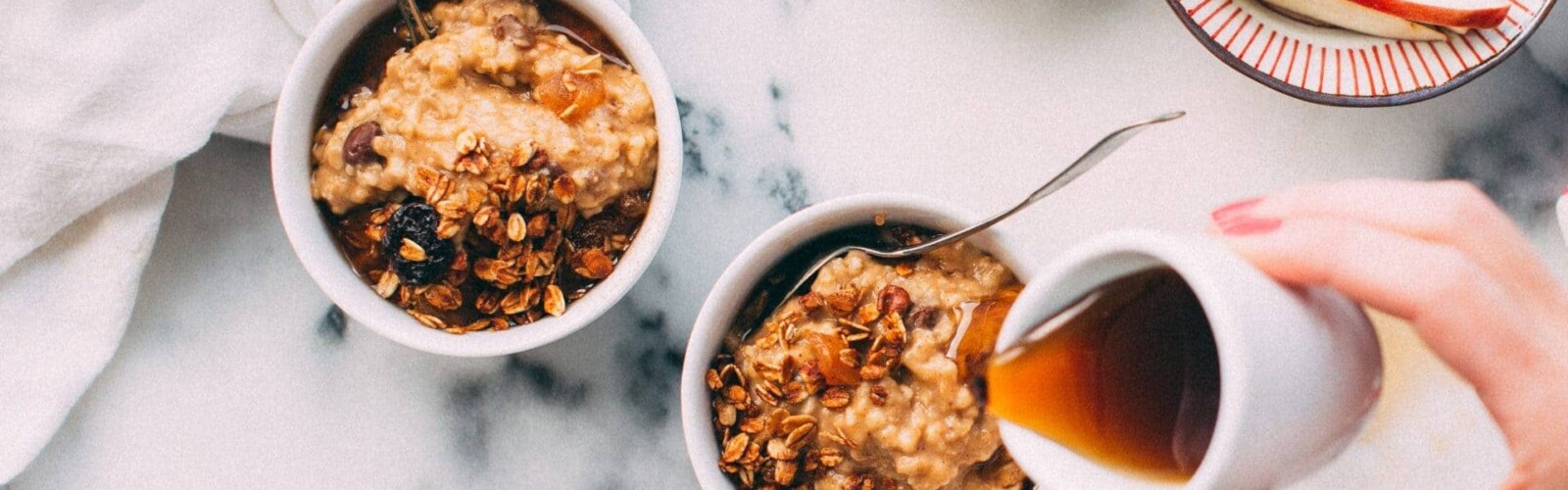 Woman pouring syrup over two small bowls of overnight oats