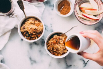 Woman pouring syrup over two small bowls of overnight oats
