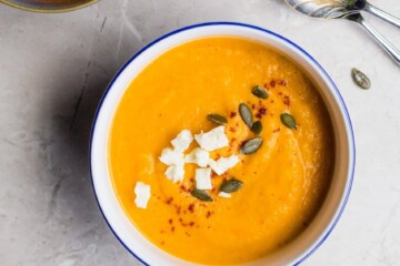 A bowl of orange carrot soup on a kitchen counter