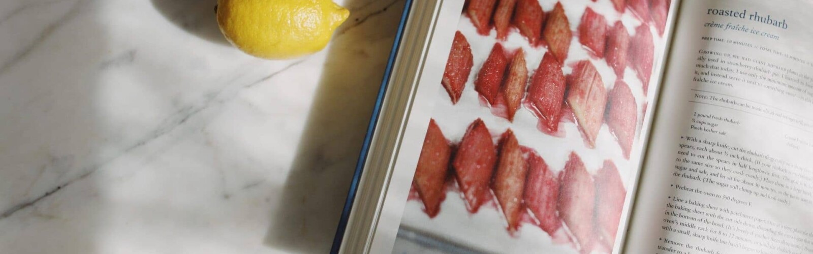 Lemons in a bowl and a cookbook open to a recipe photographed on a marble kitchen counter