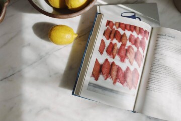 Lemons in a bowl and a cookbook open to a recipe photographed on a marble kitchen counter