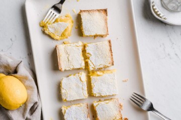 Organic and gluten free lemon bars ready-to-serve and one already nibbled on, placed on a marble counter top