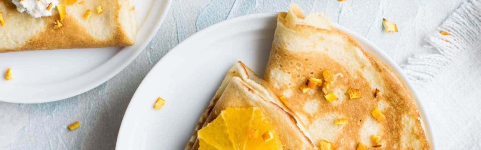 Breakfast crepes and oranges on white plate on marble kitchen counter
