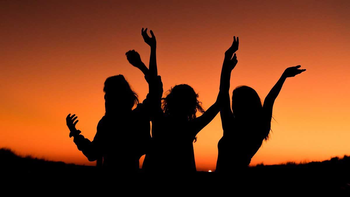 silhouette of 3 happy women against orange sky.