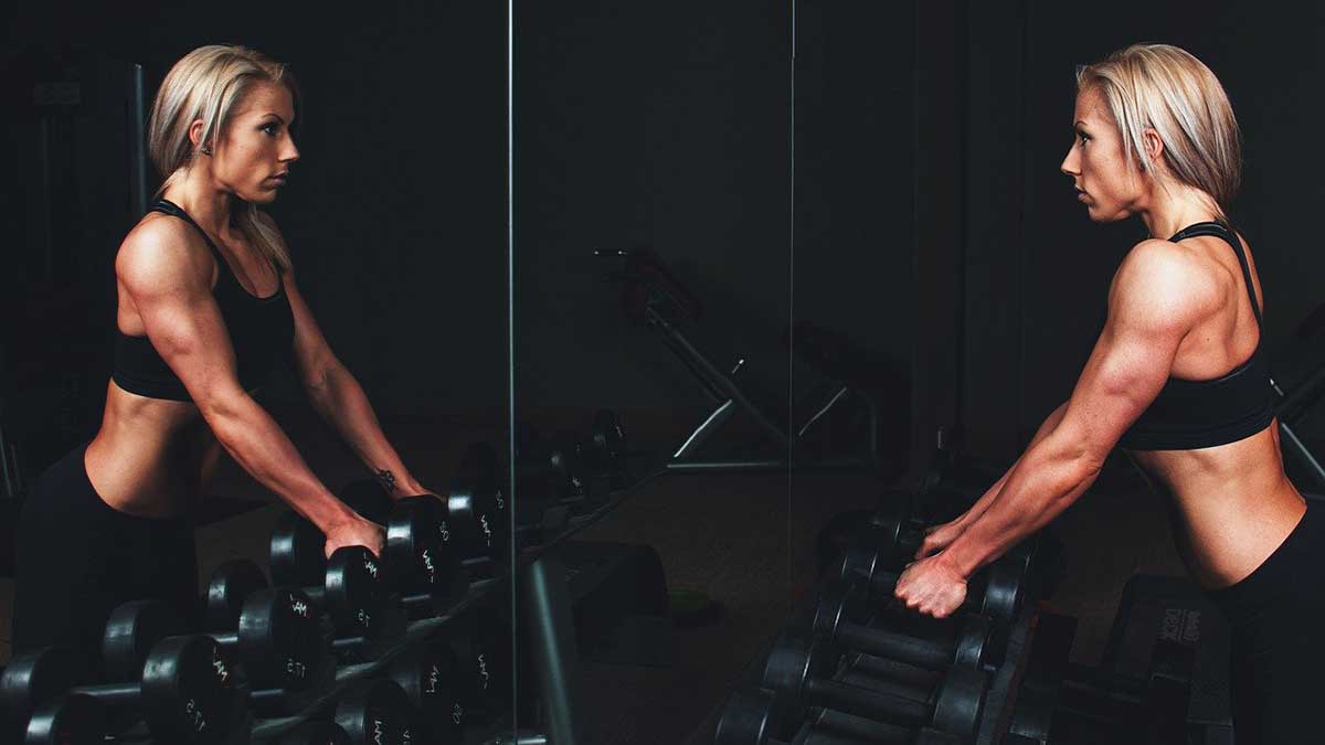 strong woman in black lifting weights against black background.