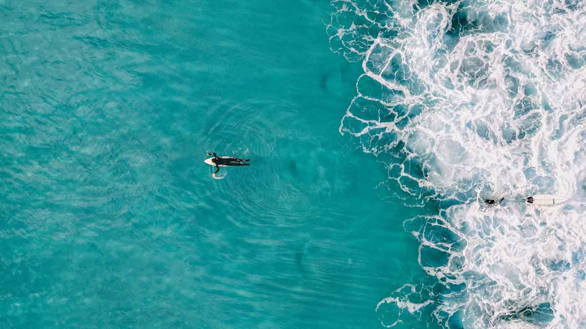 turquoise blue ocean with surfer swimming to sea.