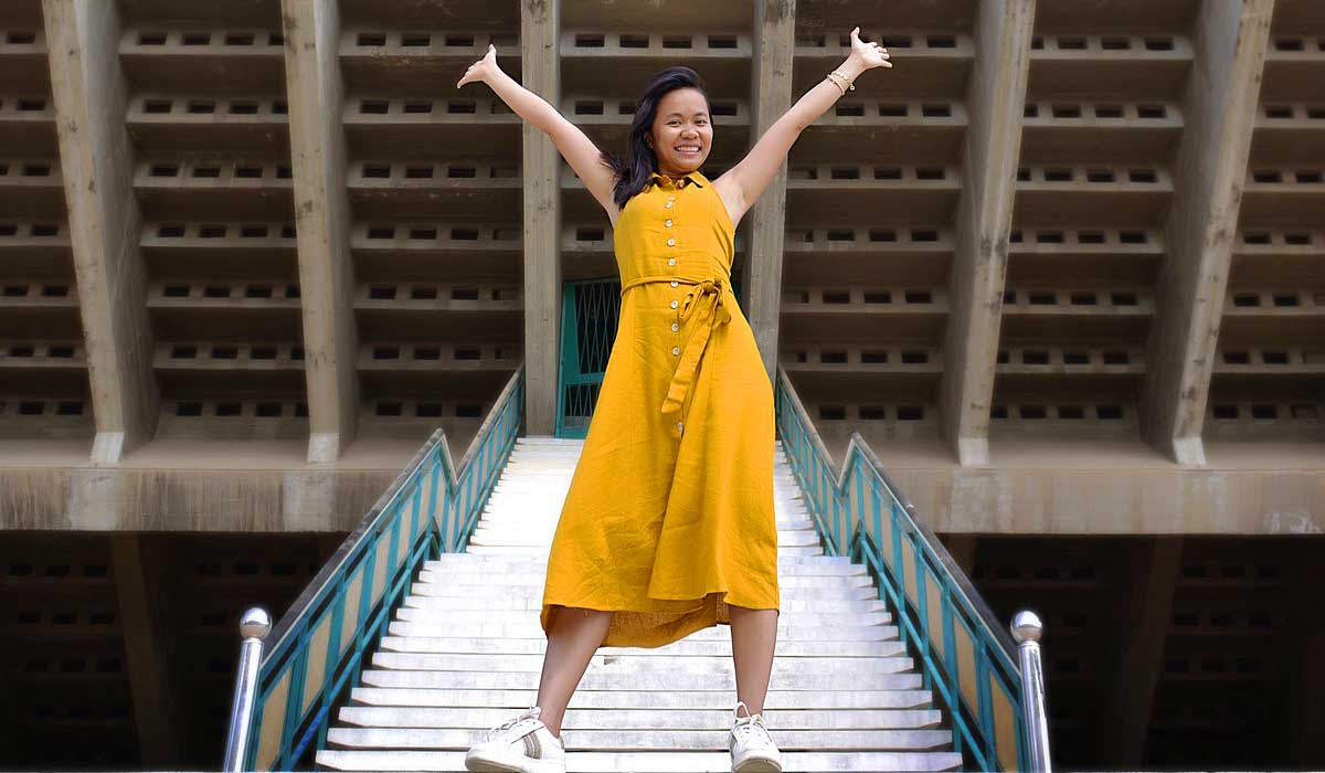 confident woman in yellw dress with upraised arms.